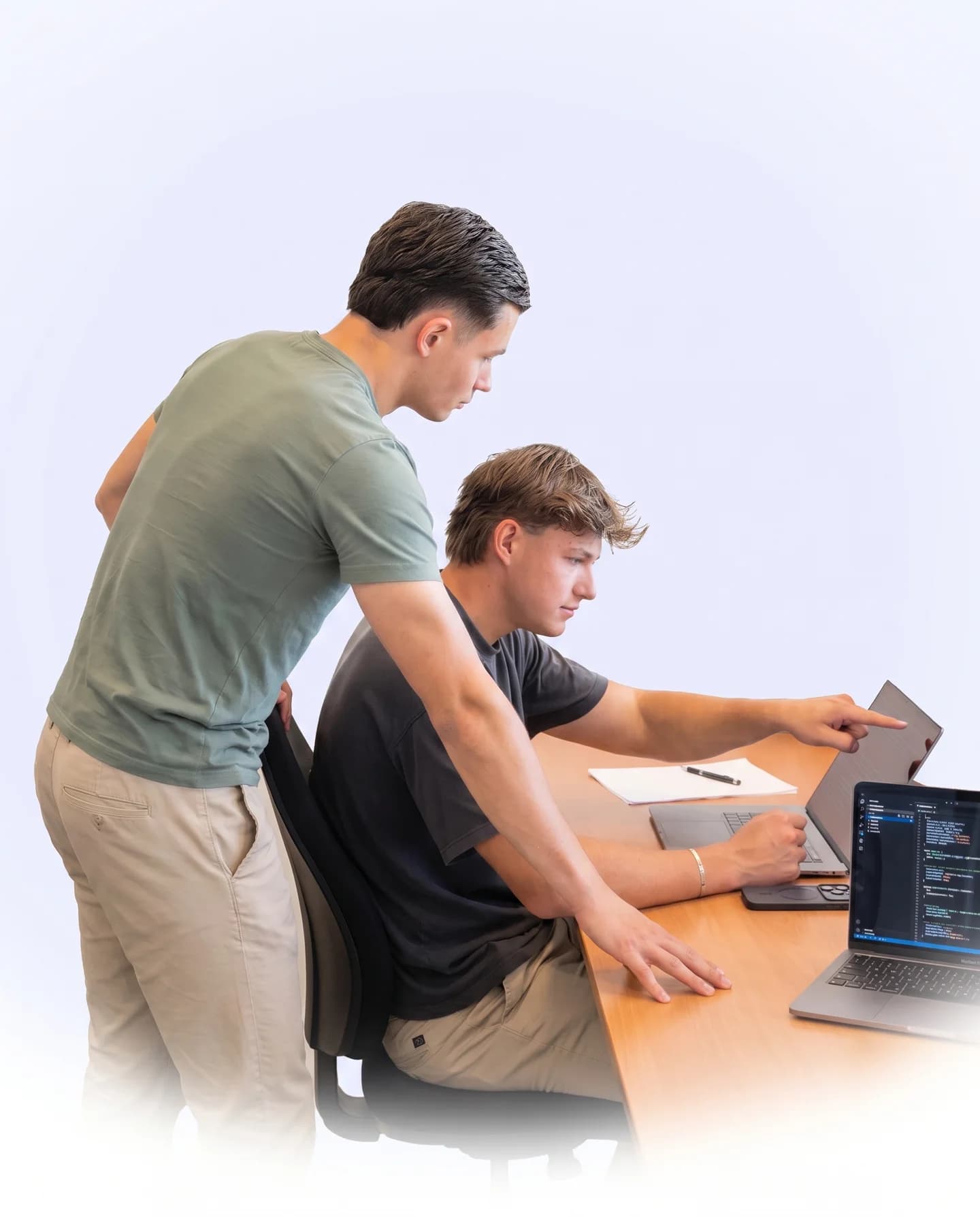 De twee oprichters van Noventis Web werken samen achter een laptop: één zit en wijst naar code op het scherm, de ander kijkt staand mee.